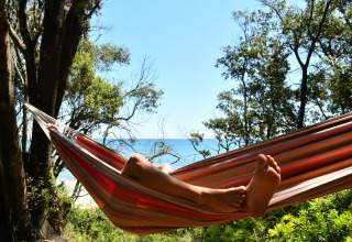 Persona che si rilassa in un'amaca tra gli alberi con vista mare al Camping Bagheera – Eco lodges Corsica.