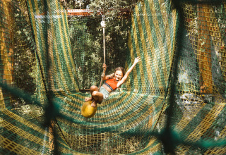 Child swings on a rope above netted adventure course at Camping Bagheera – Eco lodges Corsica, outdoors.