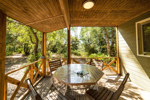Wooden porch with table and chairs surrounded by nature at Camping Bagheera – Eco lodges Corsica, glamping spot.