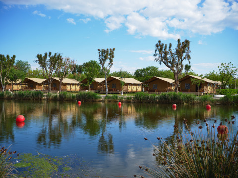 Glamping accommodation with tents by a lake and trees at Camping Nautic Almata – Glamping Costa Brava.
