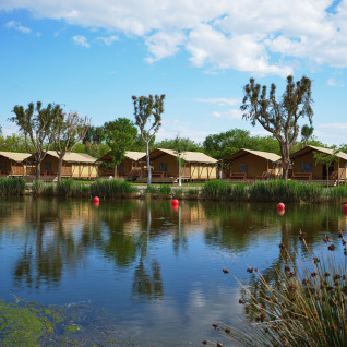 Glamping accommodation with tents by a lake and trees at Camping Nautic Almata – Glamping Costa Brava.