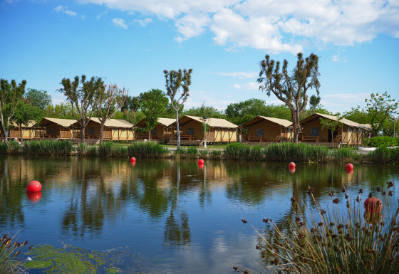 Glamping-Unterkünfte mit Zelten am See, umgeben von Bäumen bei Camping Nautic Almata – Glamping Costa Brava.