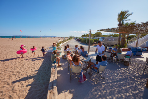 Udendørs café ved stranden på Camping Nautic Almata – Glamping Costa Brava med gæster og børn, der leger.