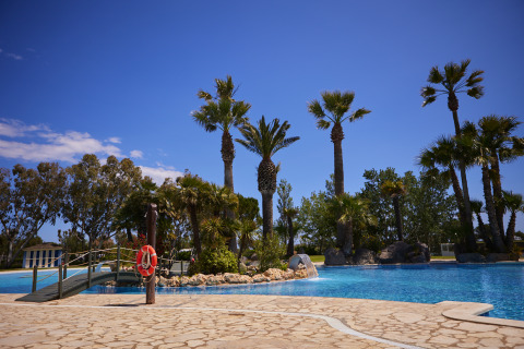 Palm-lined swimming pool under clear blue sky at Camping Nautic Almata – Glamping Costa Brava, perfect getaway.