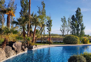 Swimmingpool mit Palmen und Gartenlandschaft bei Camping Nautic Almata – Glamping Costa Brava am Tag.