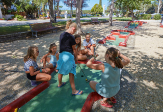 Kinderen spelen minigolf bij Camping Nautic Almata – Glamping Costa Brava, omringd door bomen en bankjes.