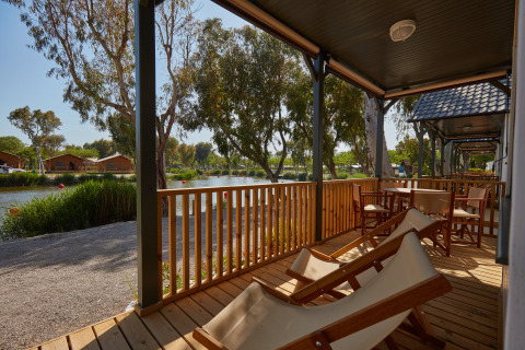Véranda en bois et chaises longues face au lac au Camping Nautic Almata – Glamping Costa Brava, Espagne.