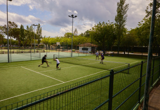 Four people are playing a tennis match on a fenced outdoor court at Camping Nautic Almata – Glamping Costa Brava.