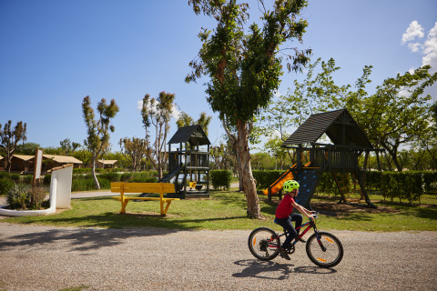 Enfant à vélo près d’une aire de jeux et tentes glamping au Camping Nautic Almata – Glamping Costa Brava.