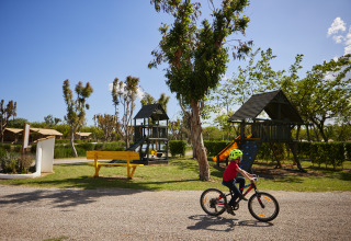 Kind fährt Fahrrad in sonnigem Spielplatzbereich bei Camping Nautic Almata – Glamping Costa Brava.