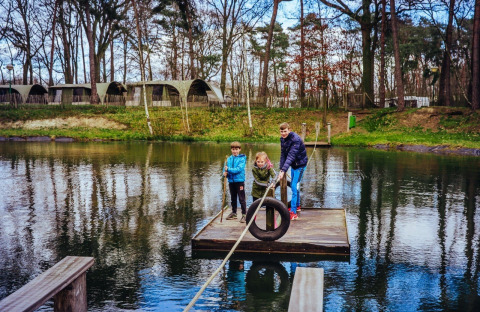 Kinderen en een volwassene op een vlot in het water, met glampingtenten op Camping Beringerzand - Finse Kota's Limburg.
