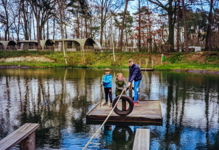 Enfants et adulte sur un radeau sur un lac, avec hébergements glamping Camping Beringerzand - Finse Kota's Limburg derrière.