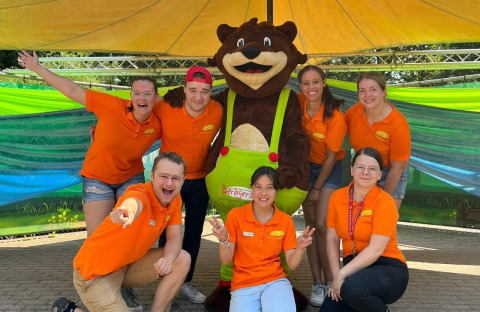 Giovani staff con magliette arancioni posano con una mascotte a Camping Beringerzand - Finse Kota's Limburg glamping.
