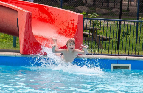 Ein Kind rutscht auf einer roten Wasserrutsche in den Pool bei Camping Beringerzand - Finse Kota's Limburg.