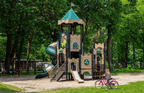 Área de juegos con temática de castillo y tobogán en Camping Beringerzand - Finse Kota's Limburg, niña en bici.