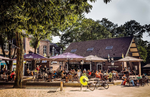Udendørs caféområde på Camping Beringerzand - Finse Kota's Limburg, med folk under parasoller og cykler.