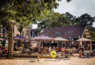 Terrace at Camping Beringerzand - Finse Kota's Limburg with guests relaxing under umbrellas and bikes parked.