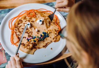 Kind eet pannenkoek versierd als gezicht met snoepjes bij Camping Beringerzand - Finse Kota's Limburg.