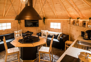 Interieur van een Finse Kota op Camping Beringerzand Limburg met grill, banken en keukenblok.