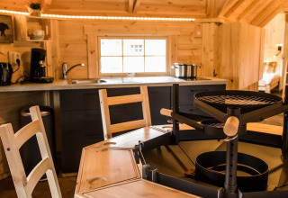 Binnenaanzicht van Finse Kota glampinghut bij Camping Beringerzand, houten inrichting en centrale grill.