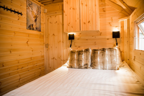 Cabane glamping chaleureuse en bois, coussins en fausse fourrure et tableau de cerf au Camping Beringerzand - Finse Kota's Limburg.