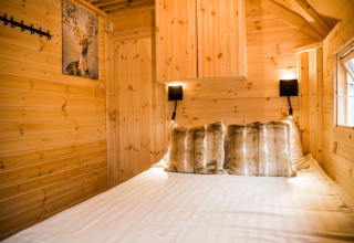 Cabane glamping chaleureuse en bois, coussins en fausse fourrure et tableau de cerf au Camping Beringerzand - Finse Kota's Limburg.