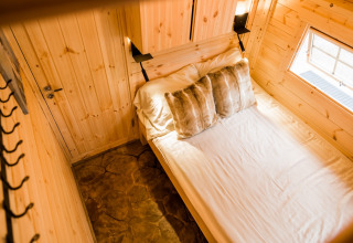 Cozy wooden interior with double bed, pillows, and window at Camping Beringerzand - Finse Kota's Limburg.