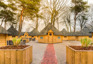 Glamping en Finse Kota en Camping Beringerzand Limburg con cabañas de madera y áreas para sentarse al aire libre.