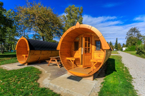 Cabañas glamping de madera en forma de barril en Camping Pilsensee, rodeadas de naturaleza y césped verde.