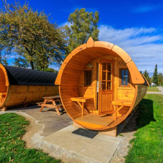 Hébergements insolites en forme de tonneaux en bois au Camping Pilsensee, installés dans un cadre verdoyant.