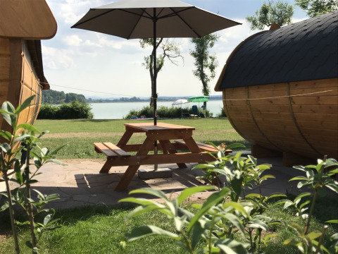 Alojamiento glamping junto al lago con cabañas de madera, mesa de picnic y paraguas en Camping Pilsensee - Wijnvaten Beieren.