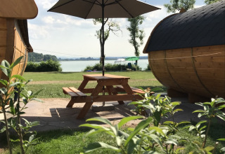 Glamping-Unterkunft am See mit Holzhütten, Picknicktisch und Sonnenschirm bei Camping Pilsensee - Wijnvaten Beieren.
