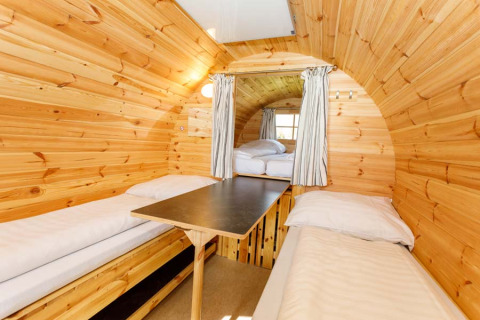 Indvendig billede af en træbeklædt glampingtønde med to enkeltsenge og bord på Camping Pilsensee.