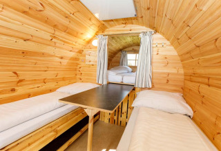 Vue intérieure d’un tonneau glamping en bois avec deux lits simples et une table au Camping Pilsensee.