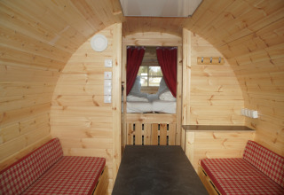 Interior de alojamiento glamping en barrica de madera en Camping Pilsensee - Wijnvaten Beieren con cama y bancos.