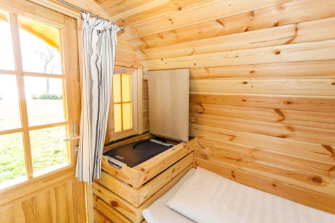 Hébergement glamping en bois au Camping Pilsensee avec lit simple, fenêtre et vue extérieure en Bavière.