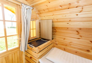 Cozy wooden glamping pod at Camping Pilsensee with single bed, storage and outdoor window view in Bavaria.