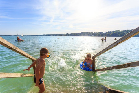 Kids playing at the lakeside dock at Camping Pilsensee - Wijnvaten Beieren on a bright sunny day.