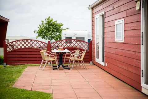 Buitenterras met vier stoelen en een tafel aan een rood huisje op Vakantiepark Ostseecamping Zierow.