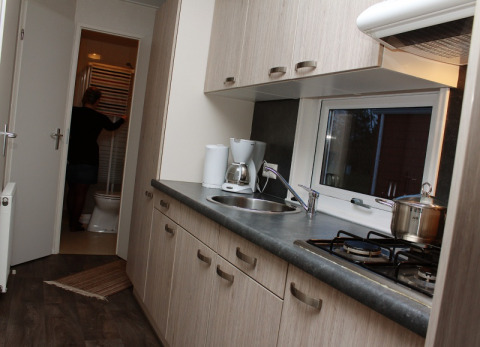 Angolo cottura moderno in una sistemazione glamping, persona che entra in bagno sullo sfondo.