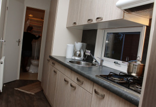 Cocina moderna en alojamiento glamping con fregadero y estufa; persona entrando al baño al fondo.