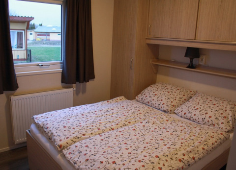 Slaapkamer met bloemendekbed in een houten huisje op Vakantiepark Ostseecamping Zierow, Duitsland.