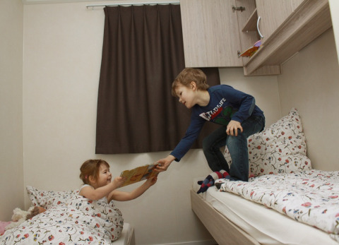 Twee kinderen spelen op gezellige bedden in een moderne lodge op Ostseecamping Zierow in Duitsland.