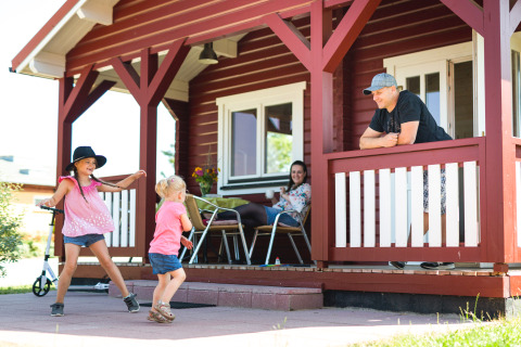 Famille prenant du bon temps devant un chalet en bois à Ostseecamping Zierow pendant que les enfants jouent.