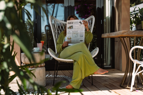Persoon ontspant bij Camping Parco Ibiza, leest krant op terras omgeven door planten.