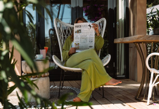 Persoon ontspant bij Camping Parco Ibiza, leest krant op terras omgeven door planten.