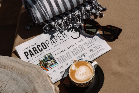 Kop koffie, zonnebril, gestreepte handdoek en Camping Parco Ibiza by San Antonio Glamping Ibiza krant op tafel.