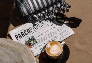 Kop koffie, zonnebril, gestreepte handdoek en Camping Parco Ibiza by San Antonio Glamping Ibiza krant op tafel.