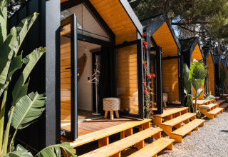 Rij moderne glampinghutten met open glazen deuren en houten traptreden bij Camping Parco Ibiza, San Antonio.