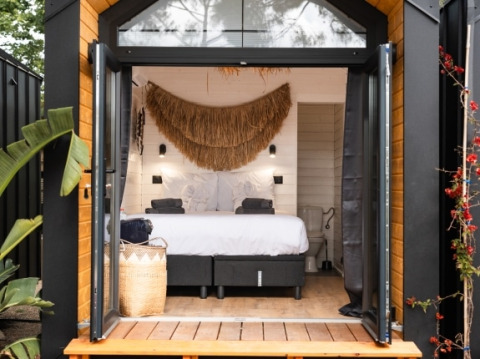 Moderne glampingaccommodatie bij Camping Parco Ibiza, met open deuren, comfortabel bed en natuurlijke decoratie.